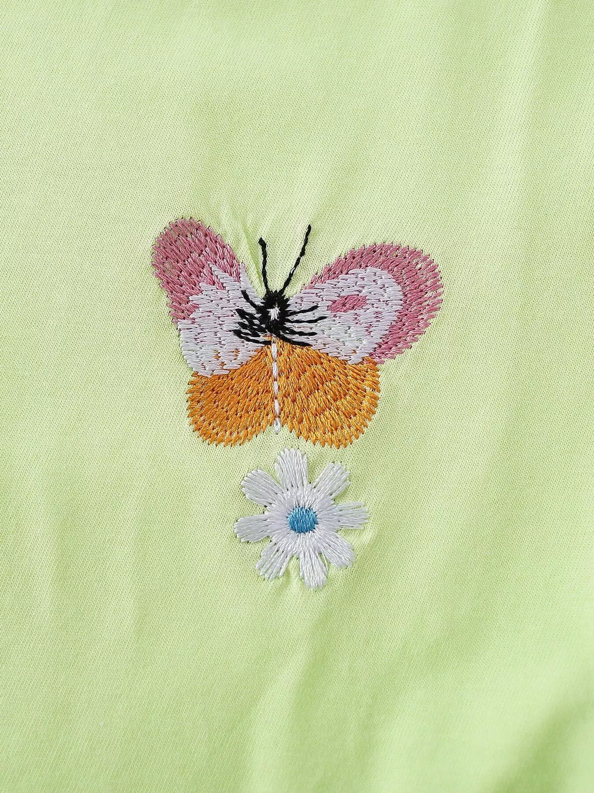Close-up of the butterfly and small blue flower embroidery on the light green top.