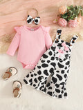 Pink baby bodysuit with black-and-white cow-print flared overalls and matching bow headband.