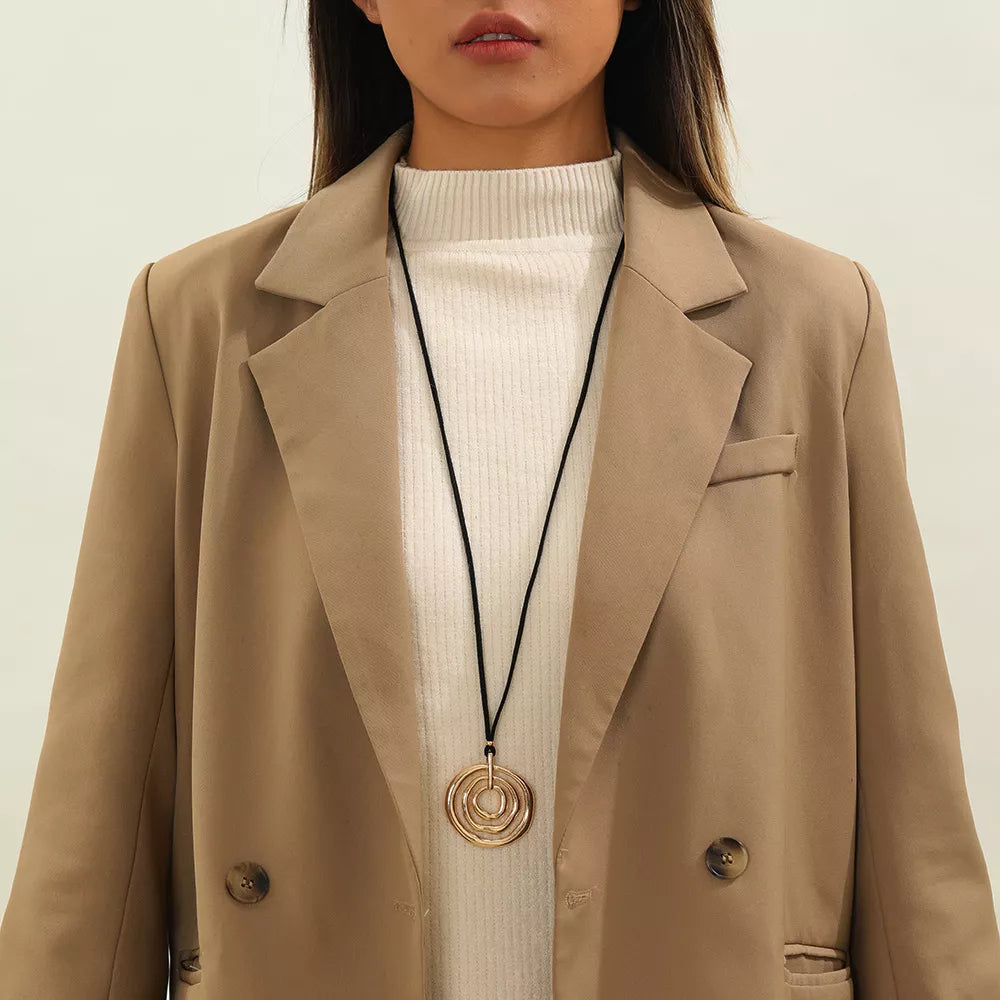 Long black cord necklace with a round gold-tone spiral pendant — detail view
