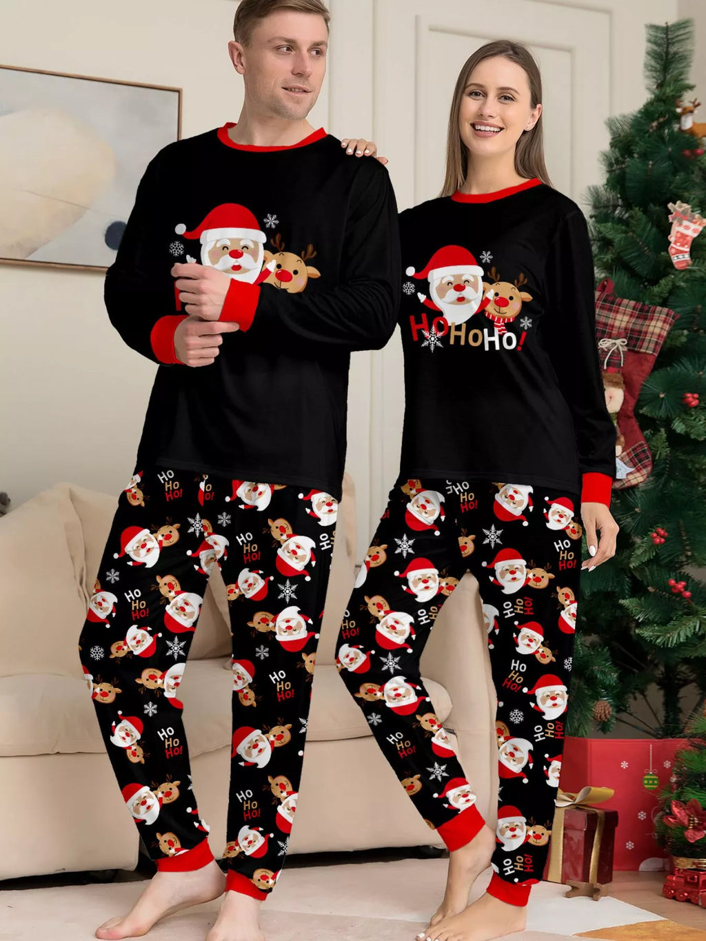 Adults modeling matching black Santa graphic tops and Santa-print pajama pants.