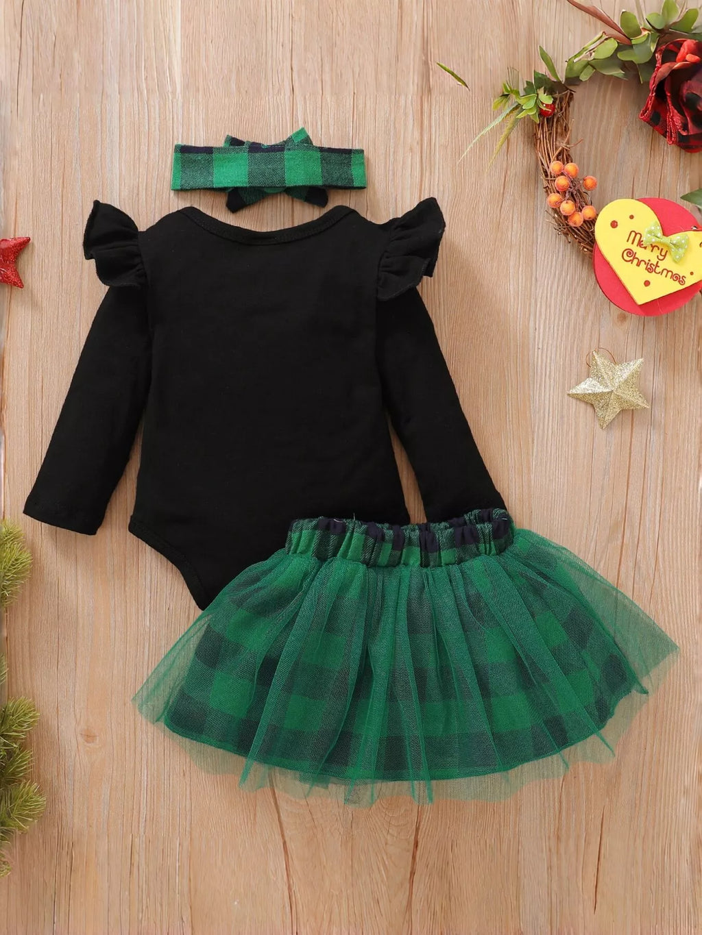 Back flat lay of a black ruffle-shoulder top, green plaid tulle skirt and green bow headband.