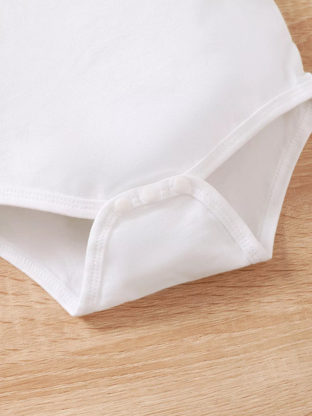 Close-up of the white bodysuit's lower hem and snap area.