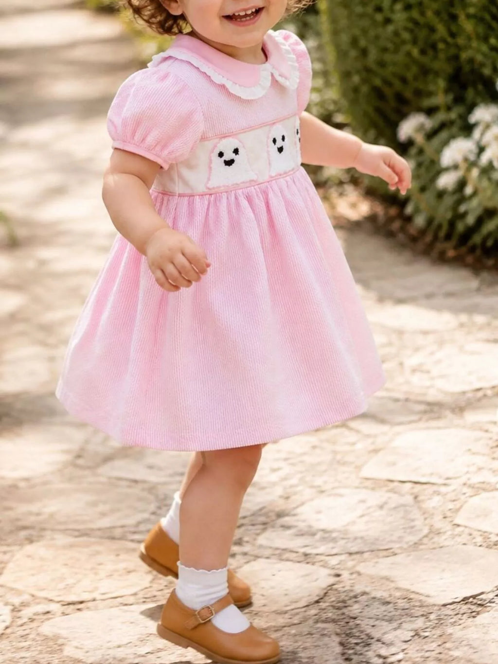 Angled view of a child wearing the pink ghost-print dress outdoors.