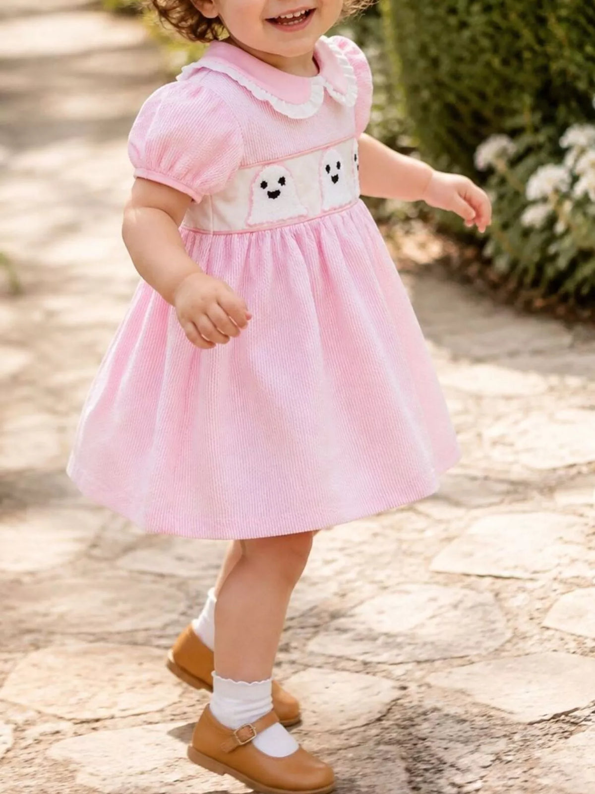 Angled view of a child wearing the pink ghost-print dress outdoors.