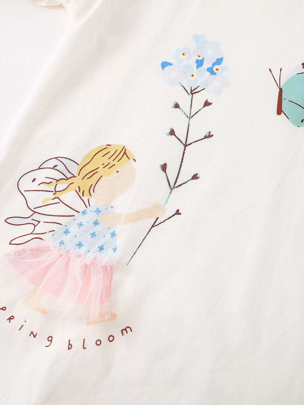 Close-up of the fairy, flower stem and butterfly artwork on the cream top.