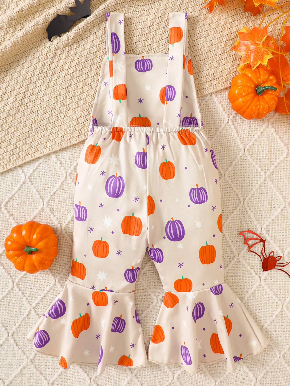 Back view of the cream orange-and-purple pumpkin-print suspender overalls.