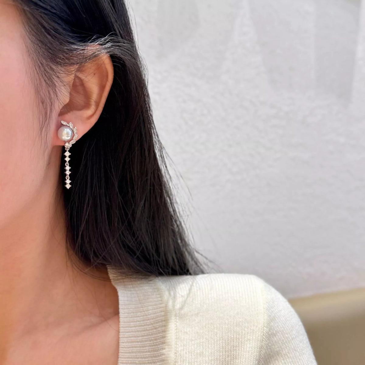 Pearl-like bead drop earrings with long dangling clear stone chains worn on a model