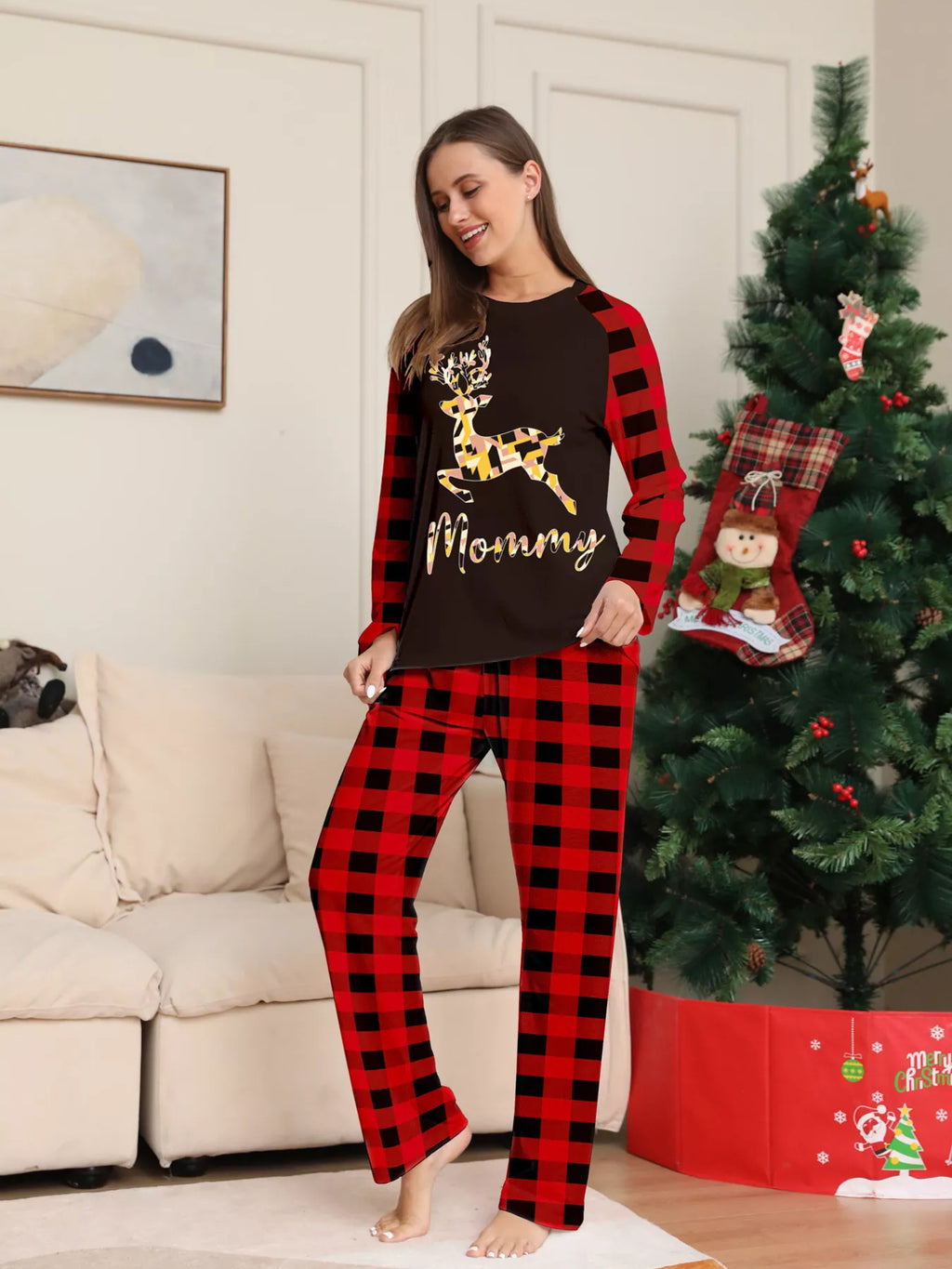 Woman modeling a black gold-tone reindeer graphic pajama top with red plaid sleeves and matching pants.