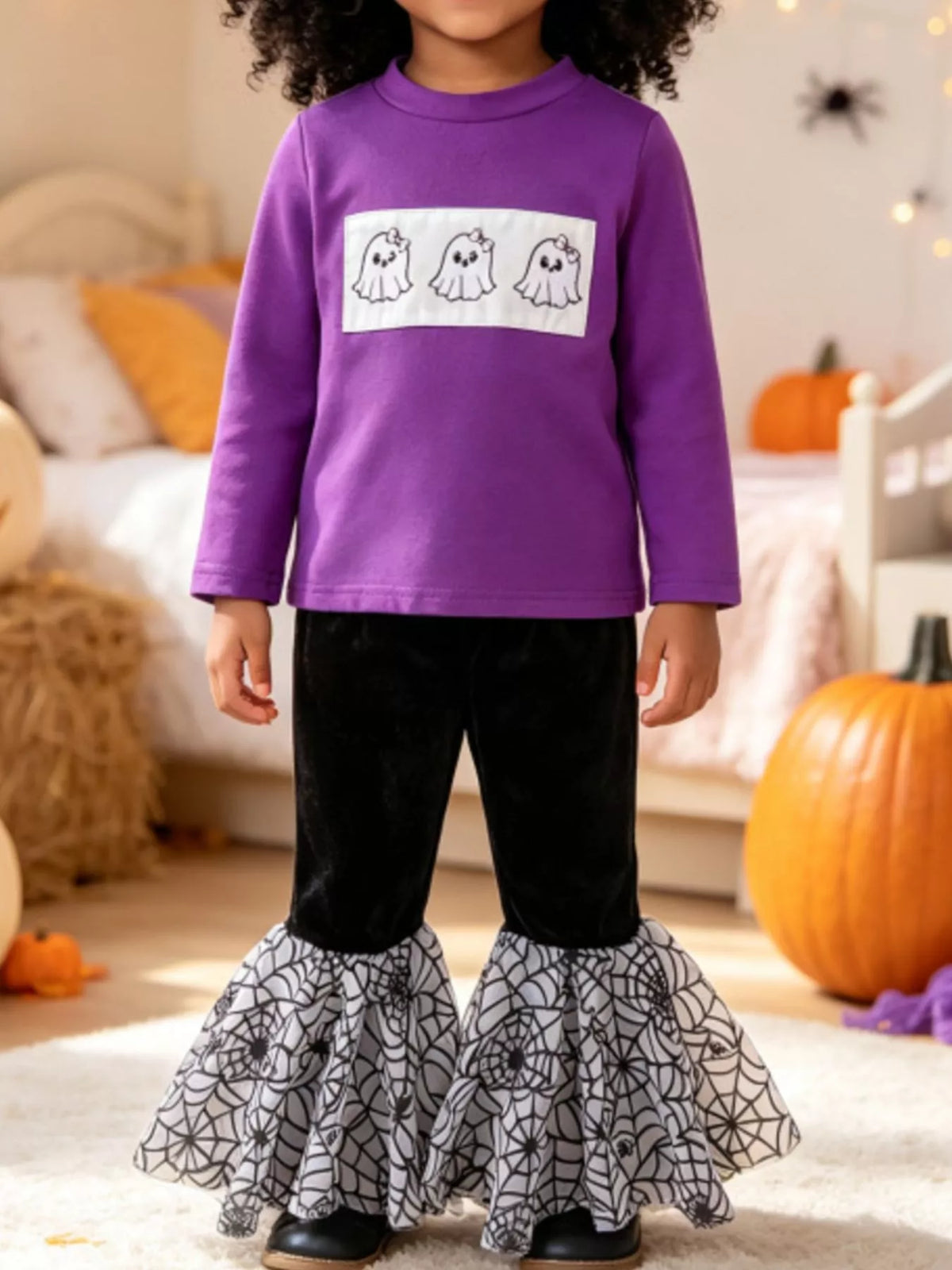Child wearing a purple ghost graphic top and black pants with gray spiderweb flared hems.