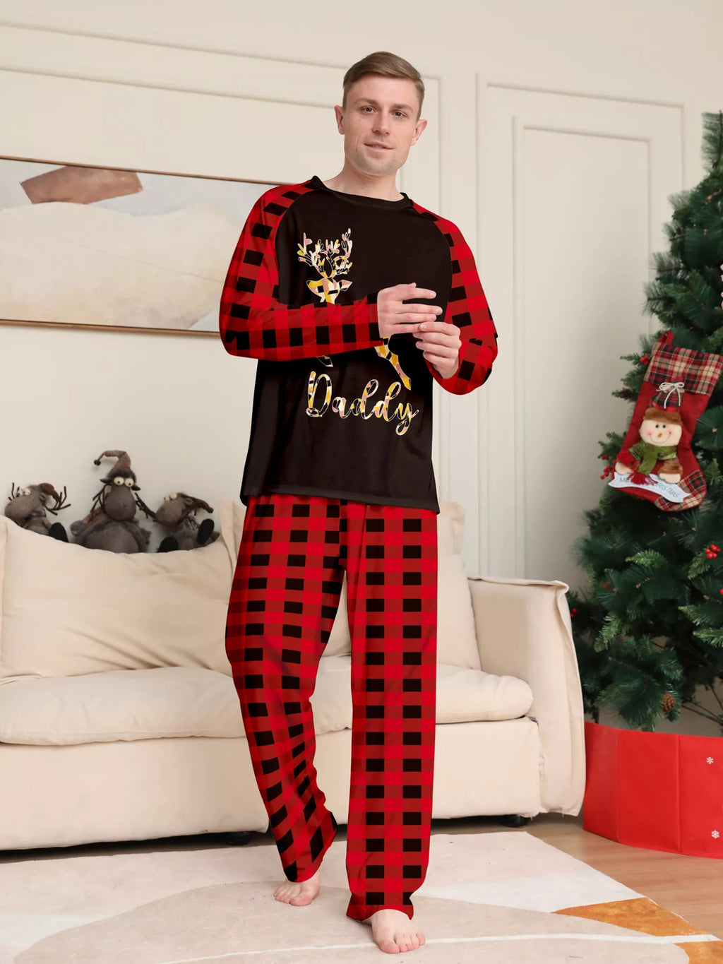 Man modeling a black gold-tone reindeer graphic pajama top with red plaid sleeves and matching pants.