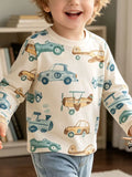 Child wearing a cream long-sleeve top printed with blue cars and tan airplanes.