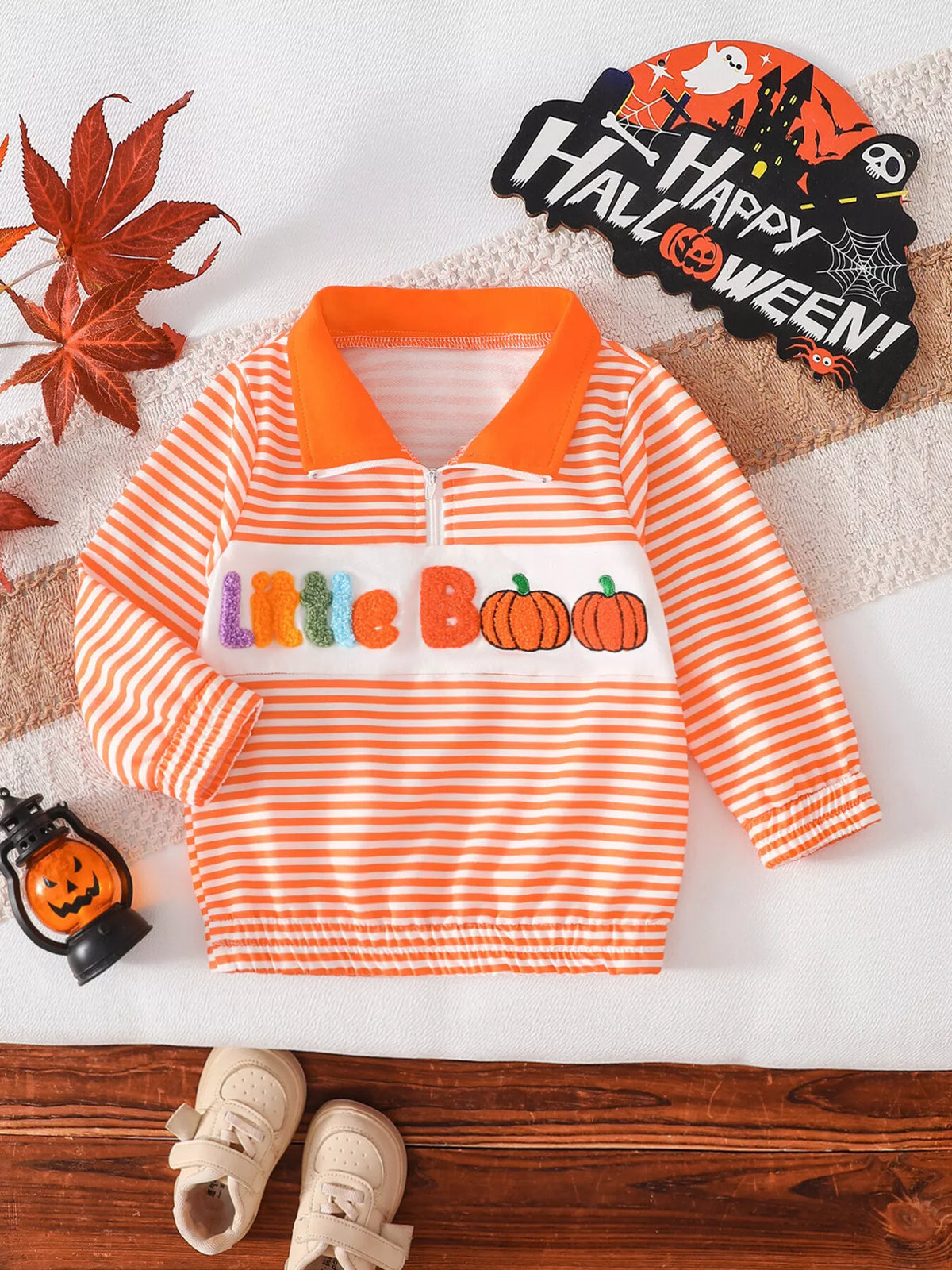 Orange-and-white striped half-zip children's top with orange collar and Little Boo pumpkin graphic.