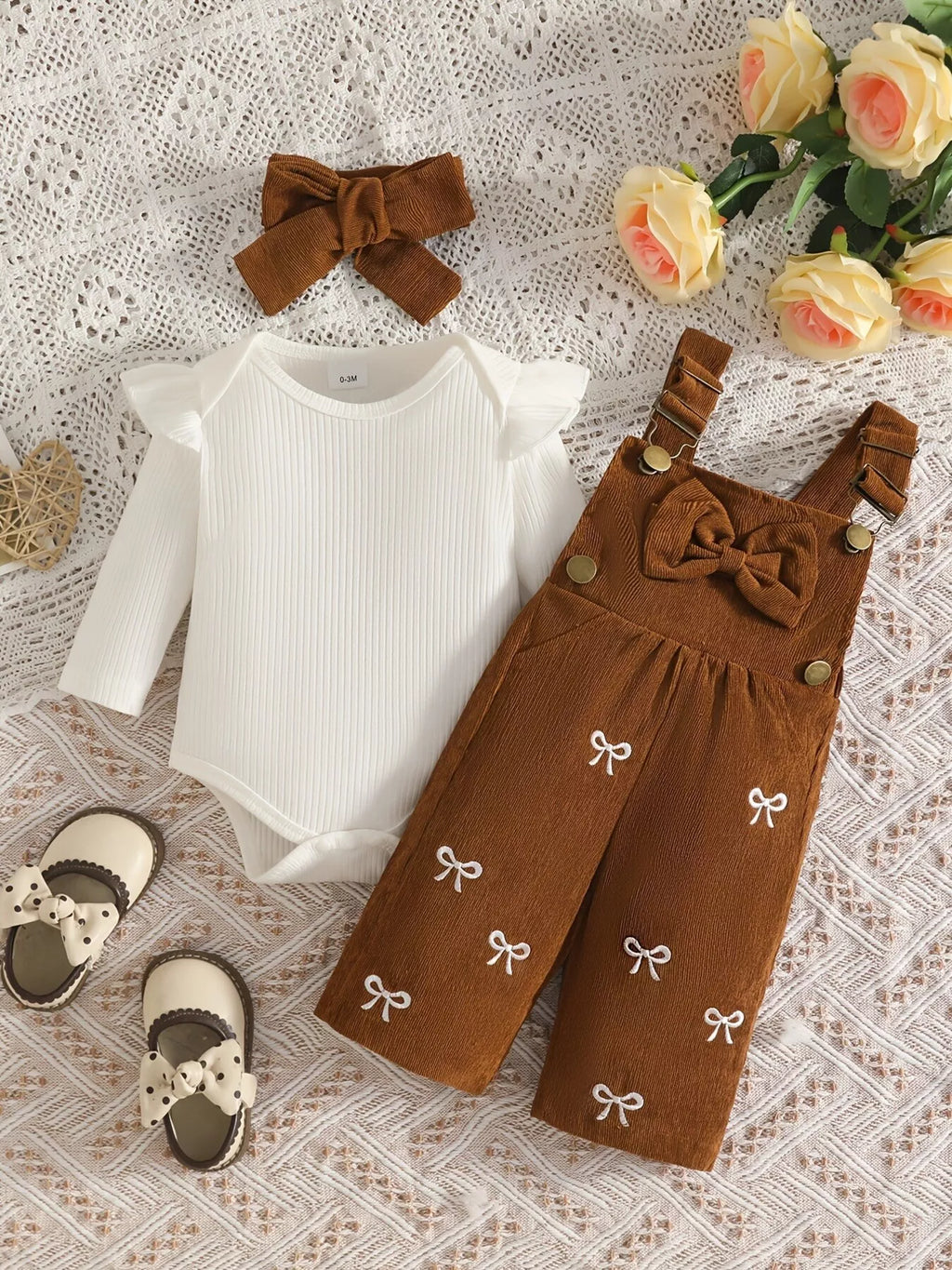 White ribbed baby bodysuit with brown bow-embroidered overalls and matching headband displayed flat