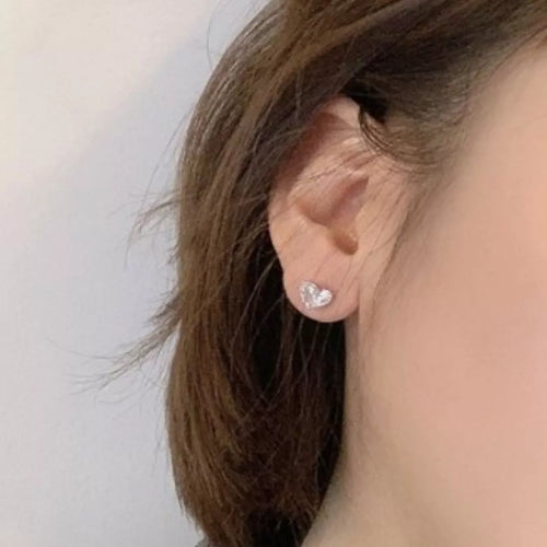 Silver-tone heart-shaped clear stone stud earrings worn on a model