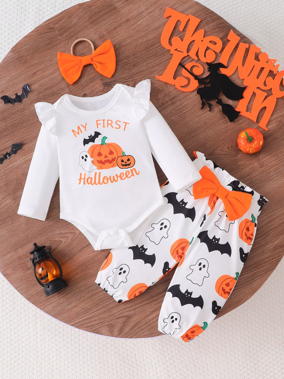 White My First Halloween baby bodysuit with pumpkin-and-ghost pants and orange bow headband.