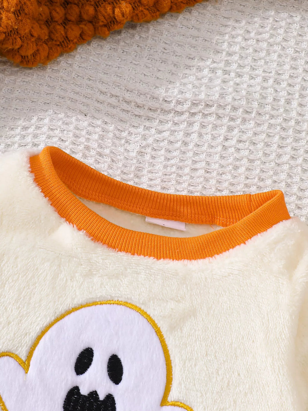 Orange crew neckline and white ghost graphic on the cream top