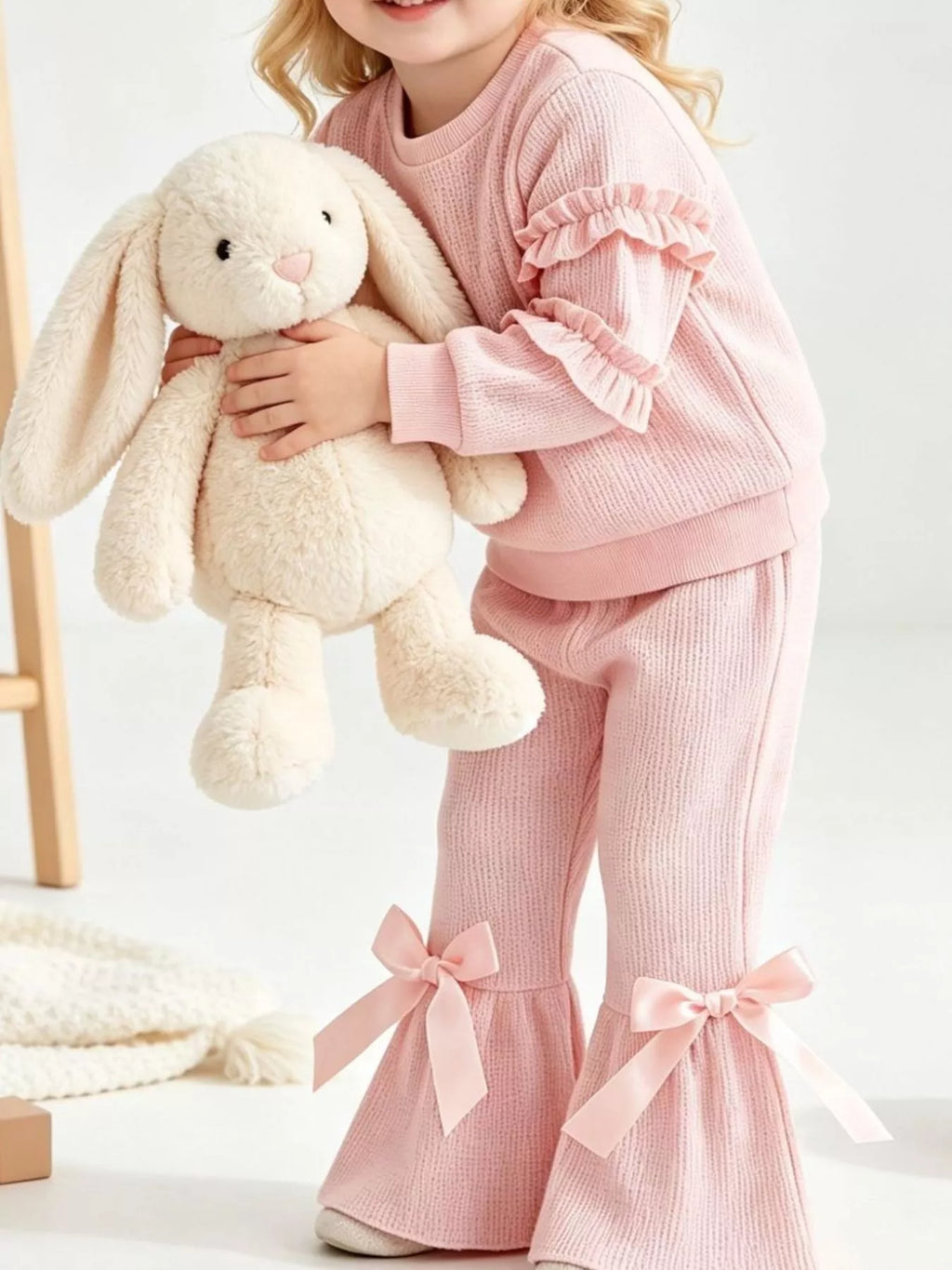 Pink ruffle-sleeve sweatshirt and bow-accented flared pants worn by a child