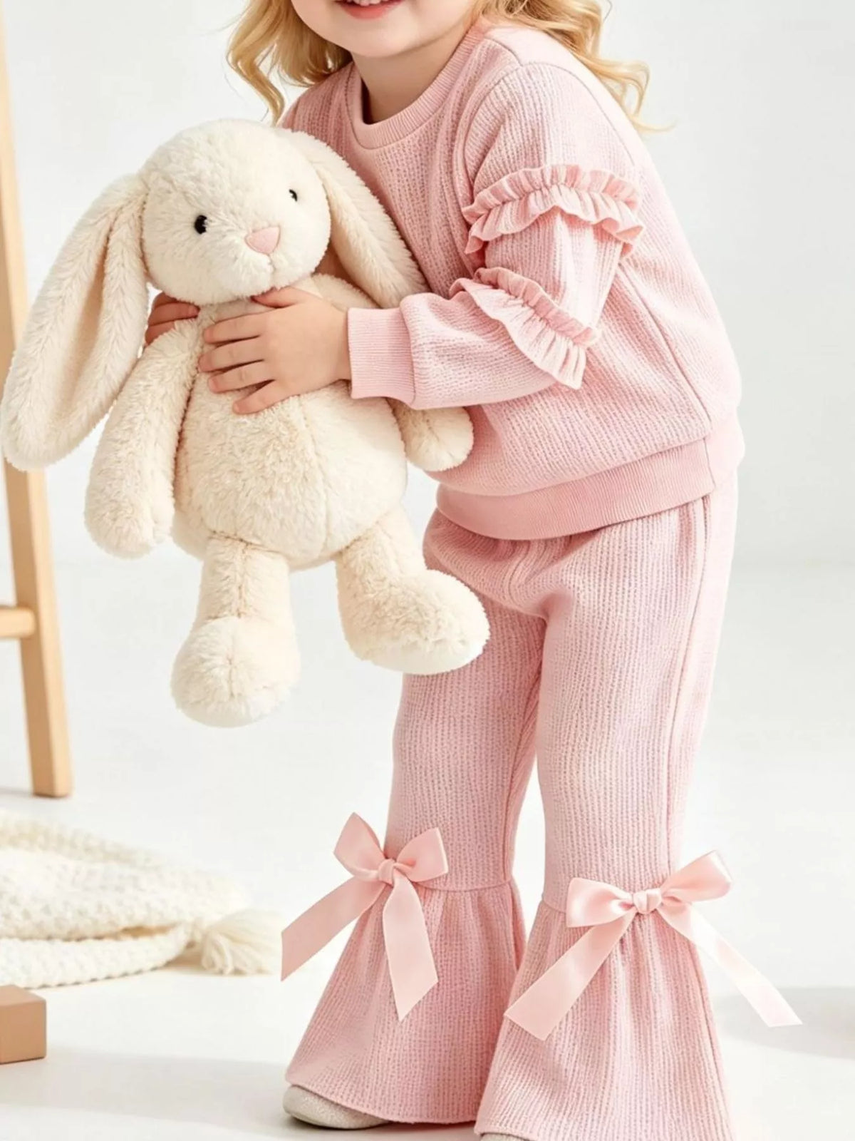 Pink ruffle-sleeve sweatshirt and bow-accented flared pants worn by a child