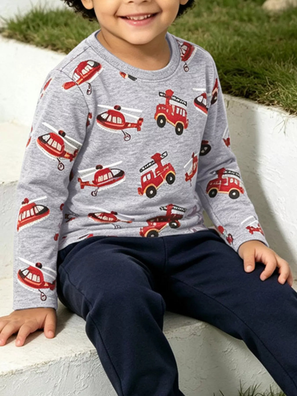 Seated child wearing the gray fire truck and helicopter print shirt.