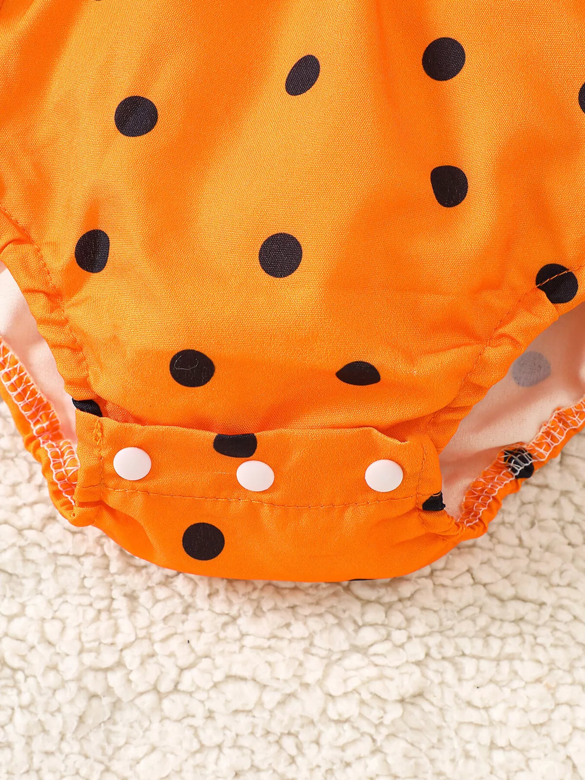 Close-up of the orange baby romper's bottom snap fastening.