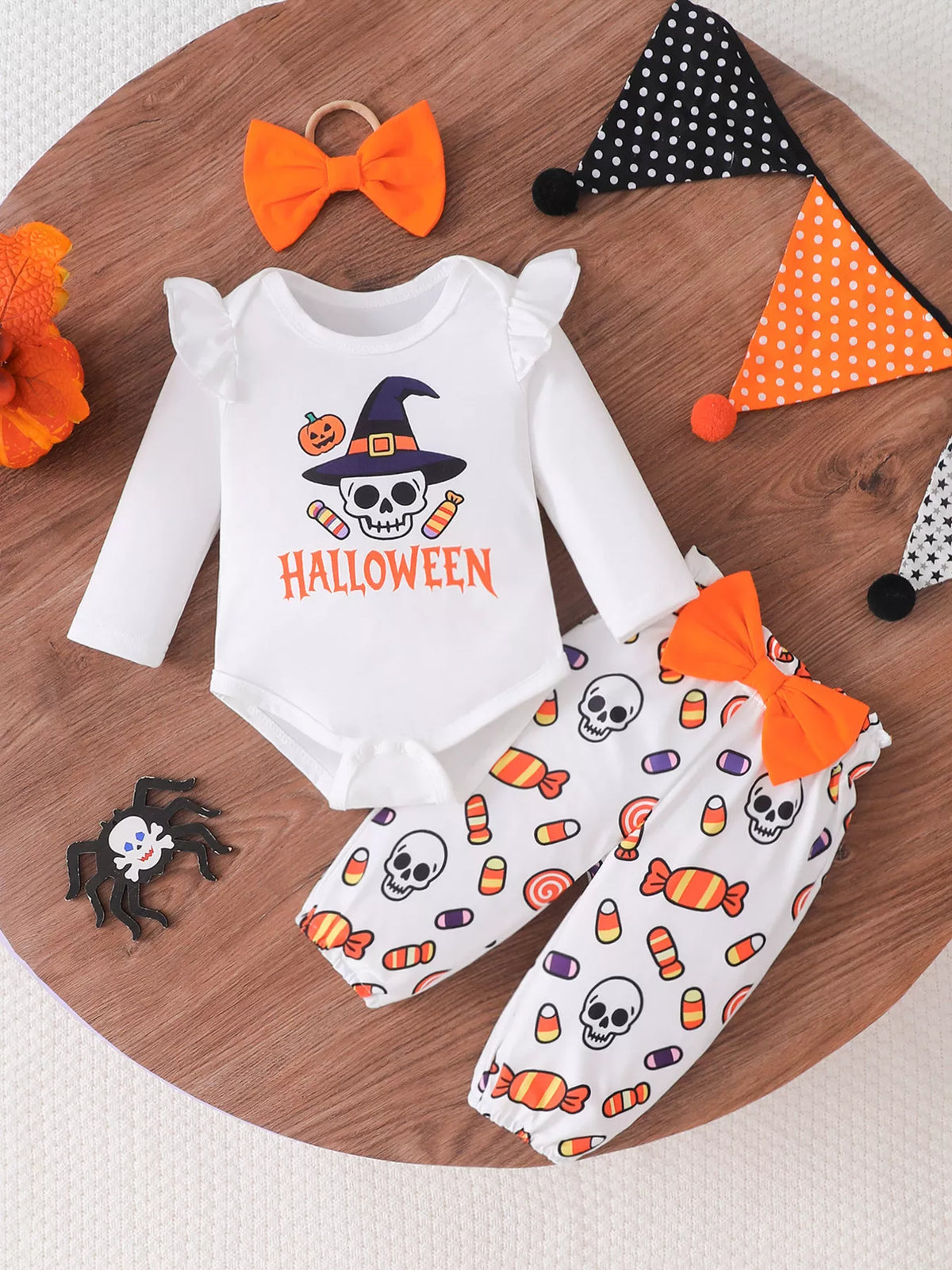White Halloween skull graphic baby bodysuit, candy-print pants and orange bow headband.