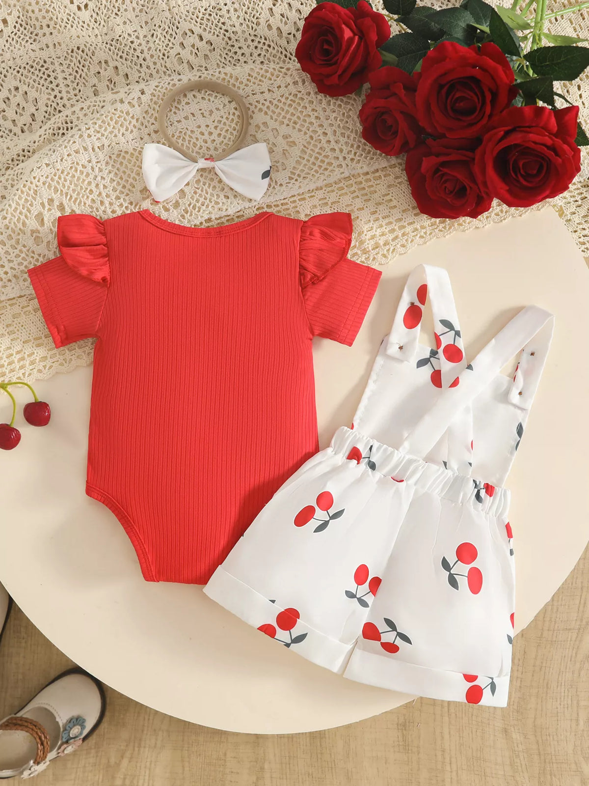 Back flat lay of the red bodysuit, white cherry-print short overalls and bow headband.