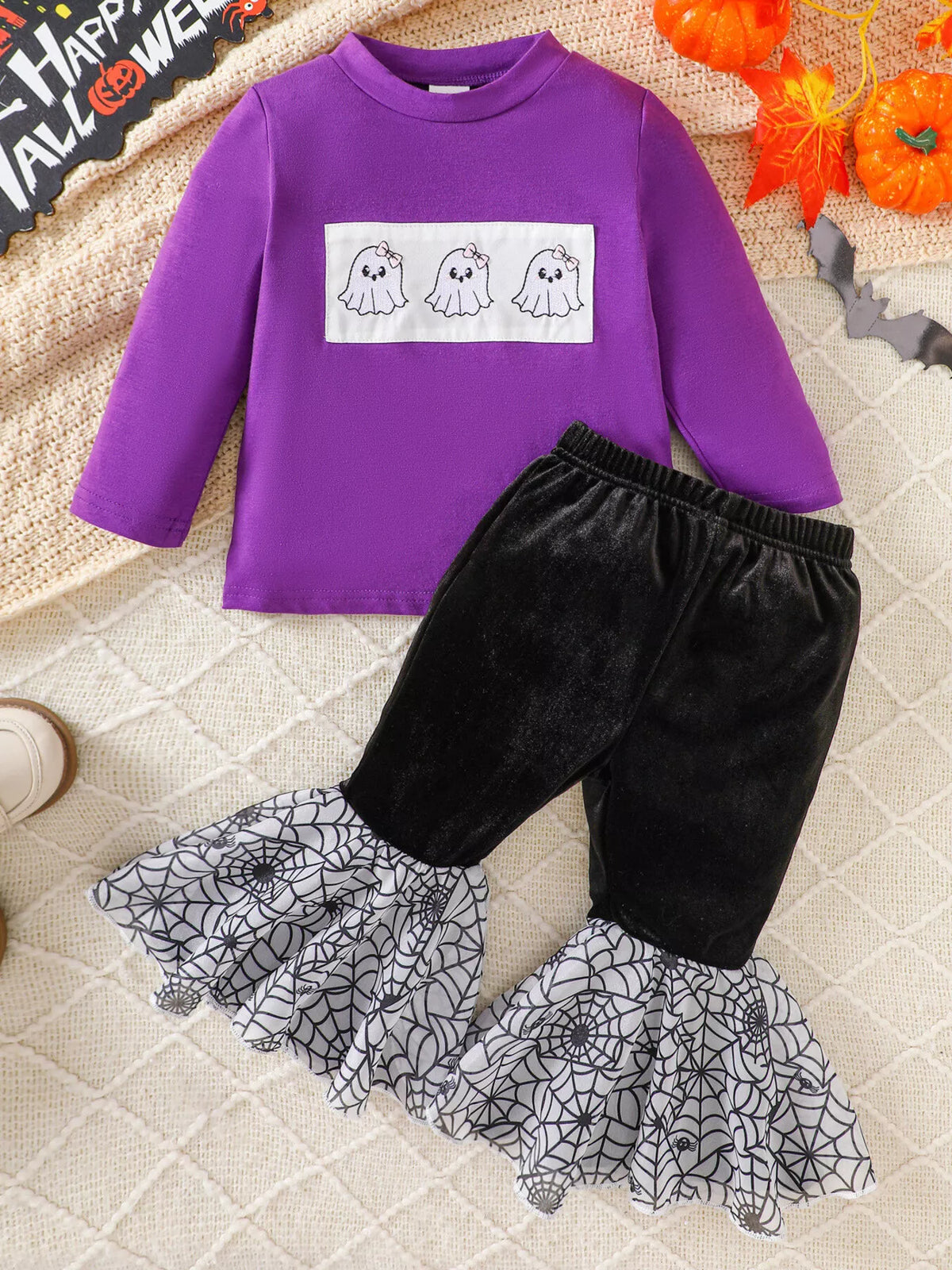 Flat lay of the purple three-ghost top and black spiderweb-hem pants.