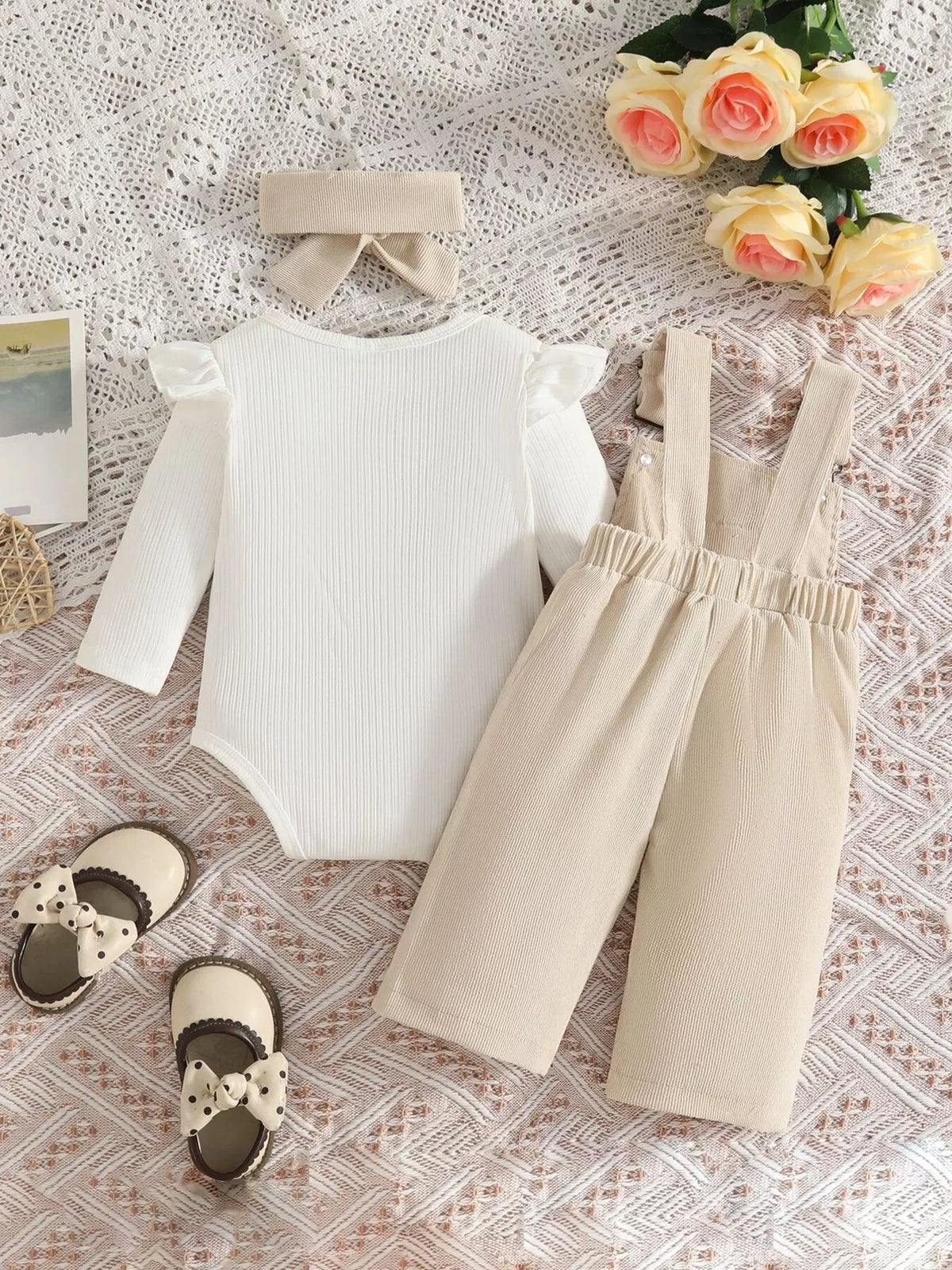 White ribbed baby bodysuit with beige bow-embroidered overalls and matching headband displayed flat