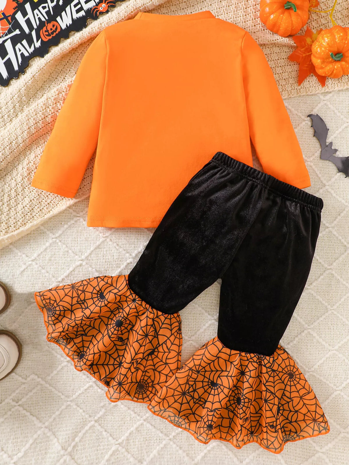 Back flat lay of the orange top and black pants with orange spiderweb flares.