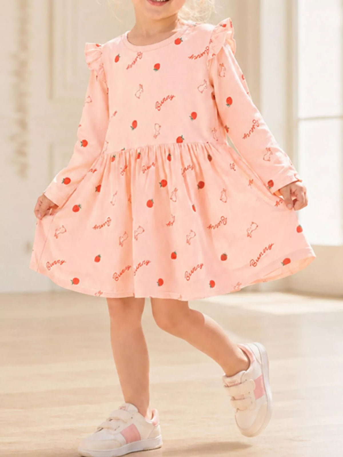 Child wearing a pink long-sleeve strawberry-and-bunny print dress with shoulder ruffles.
