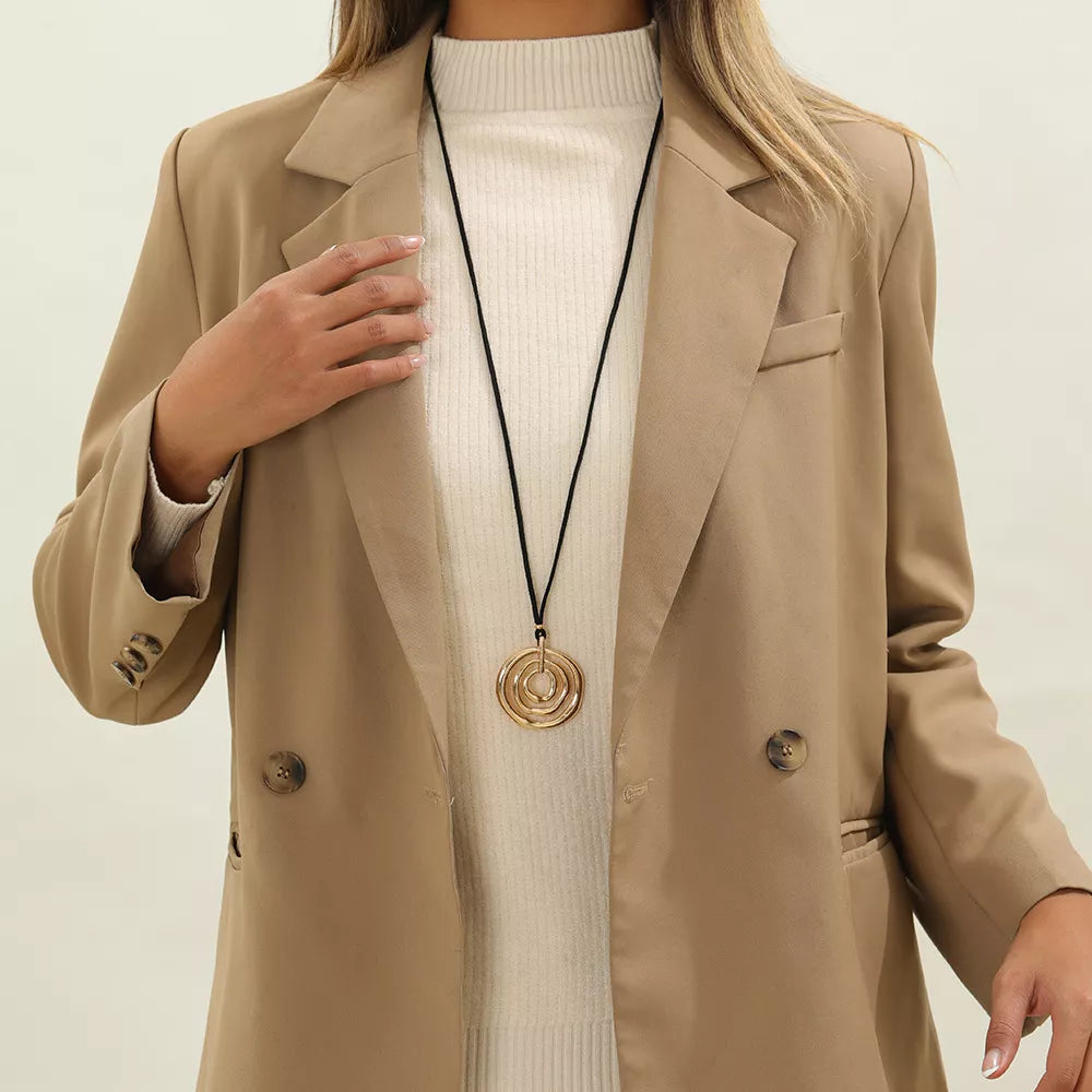 Long black cord necklace with a round gold-tone spiral pendant — detail view