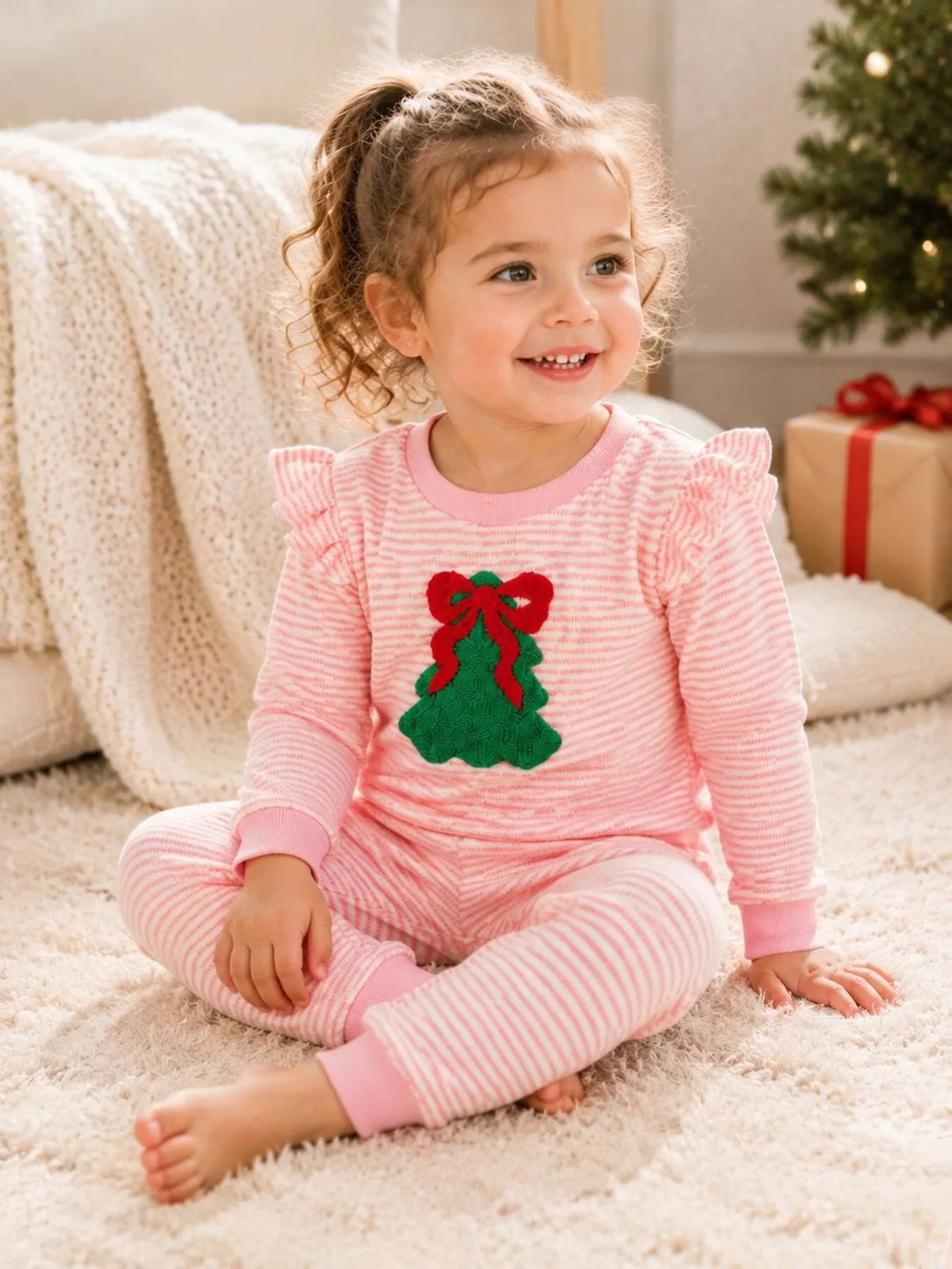 Pink striped Christmas-tree patch pajama top and ruffle-trim pants worn by a child