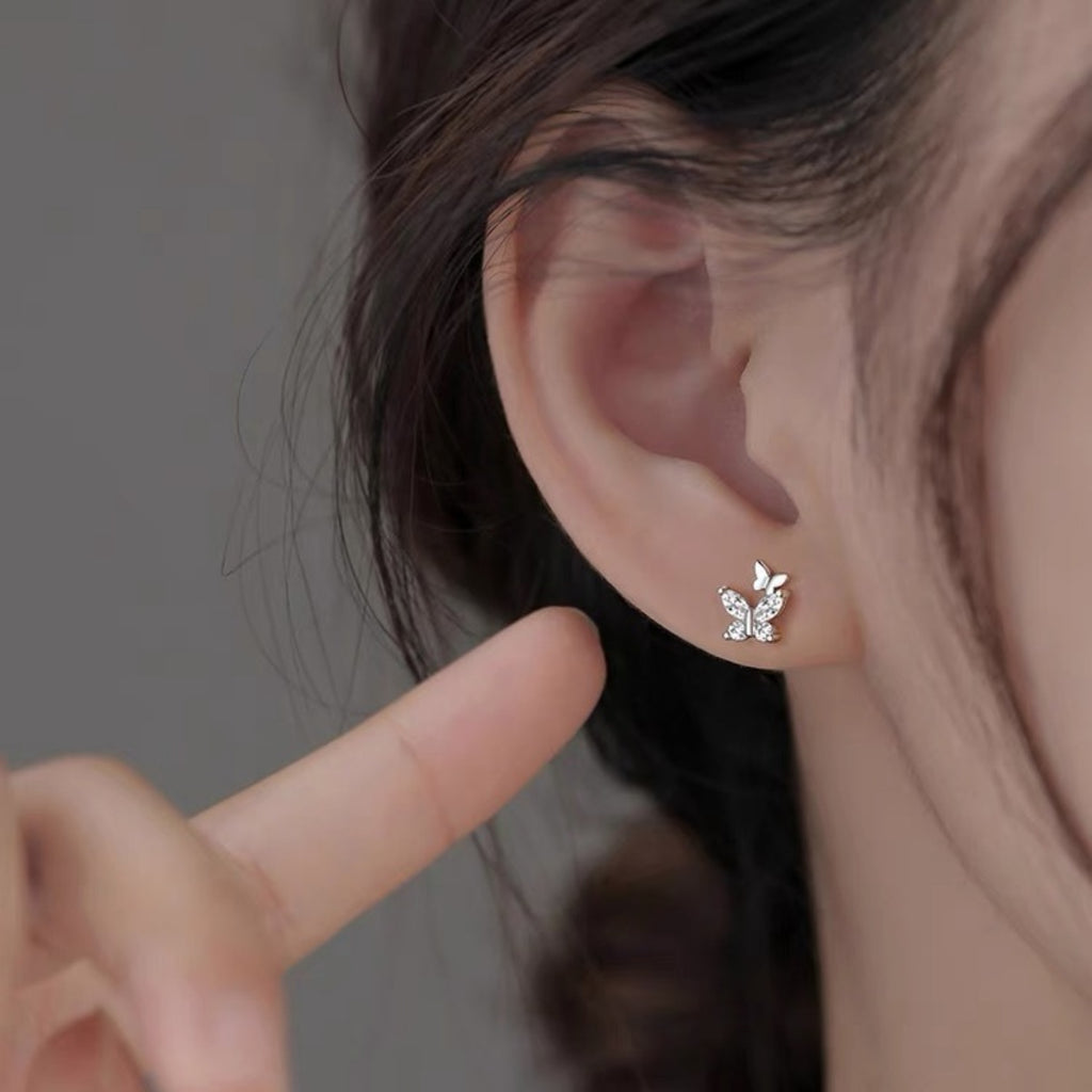 Silver-tone butterfly stud earrings with clear stones worn on a model