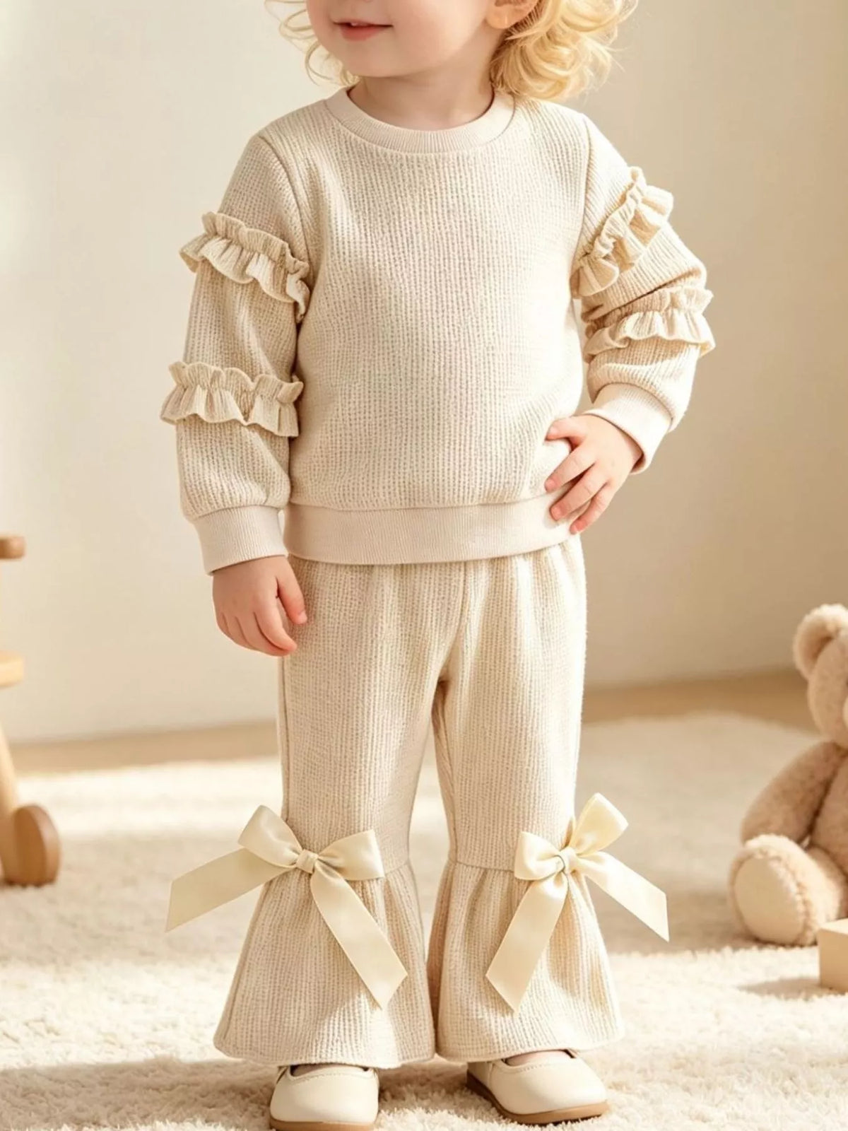 Cream ruffle-sleeve sweatshirt and bow-accented flared pants worn by a child