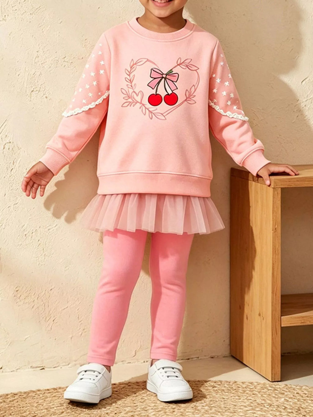 Child wearing a pink cherry-and-bow graphic sweatshirt with a tulle hem and matching pink leggings.