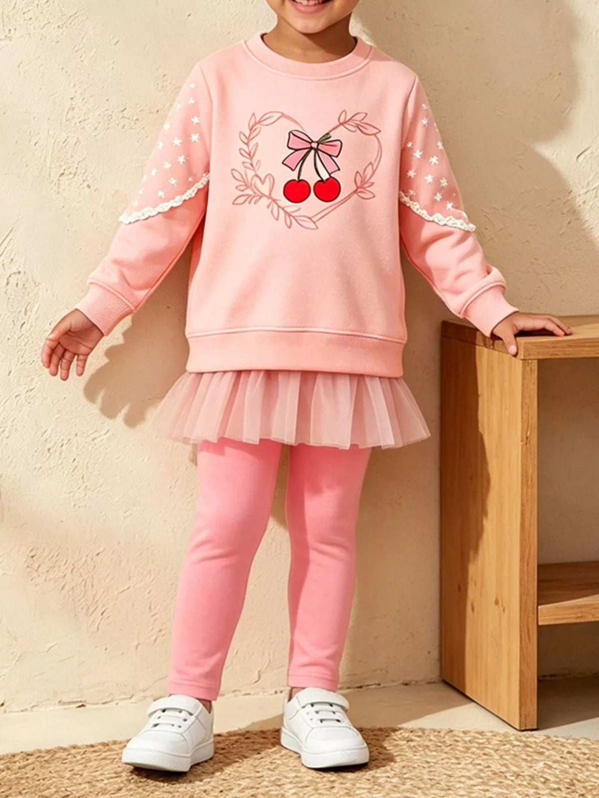 Child wearing a pink cherry-and-bow graphic sweatshirt with a tulle hem and matching pink leggings.