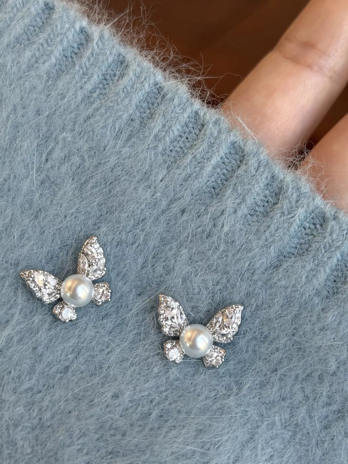 Butterfly-shaped pearl-like bead and clear stone stud earrings — detail view