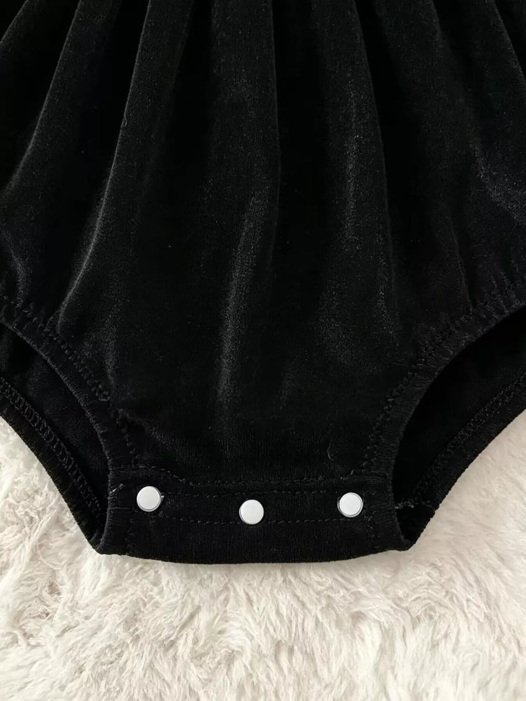 Close-up of the black baby romper's three bottom snaps.
