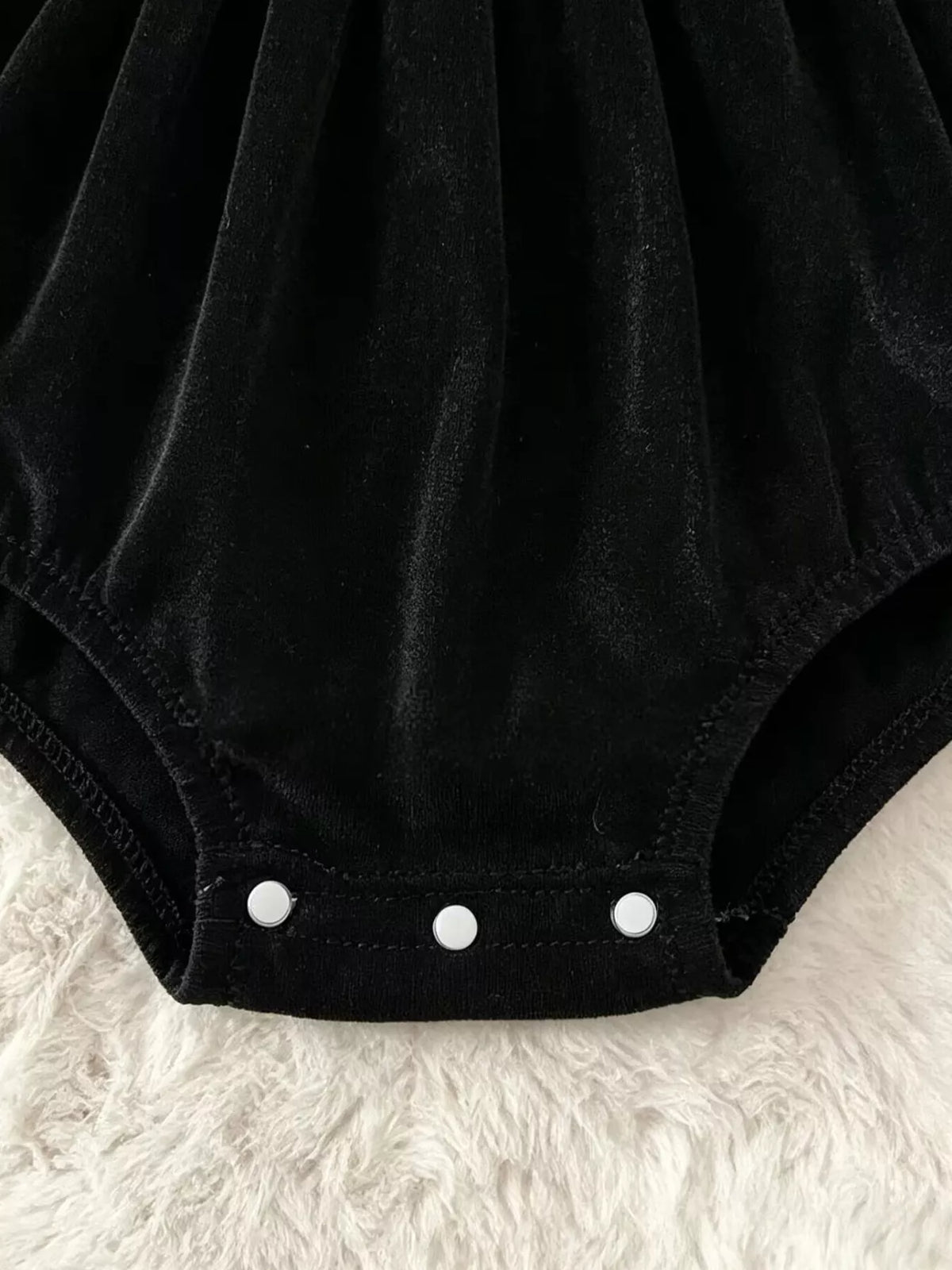 Close-up of the black baby romper's three bottom snaps.