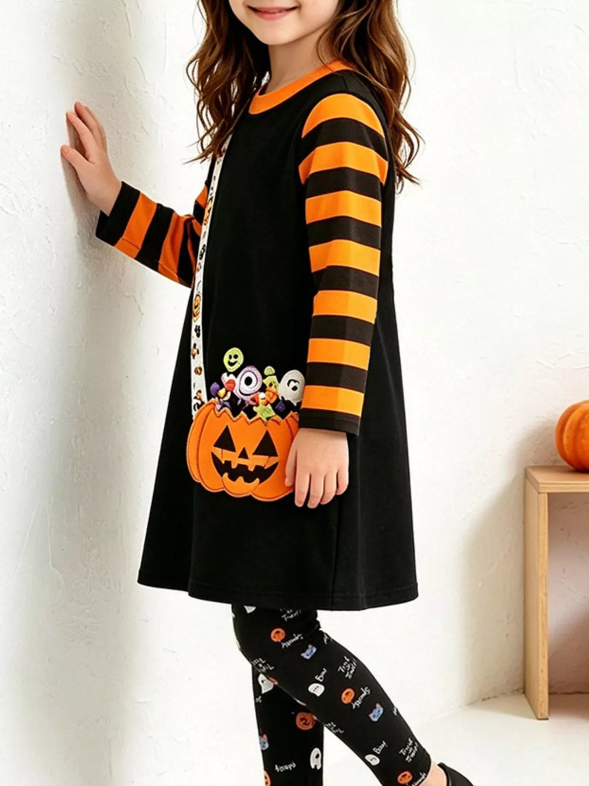 Children’s black pumpkin-print tunic with orange-striped sleeves and patterned leggings worn by a child