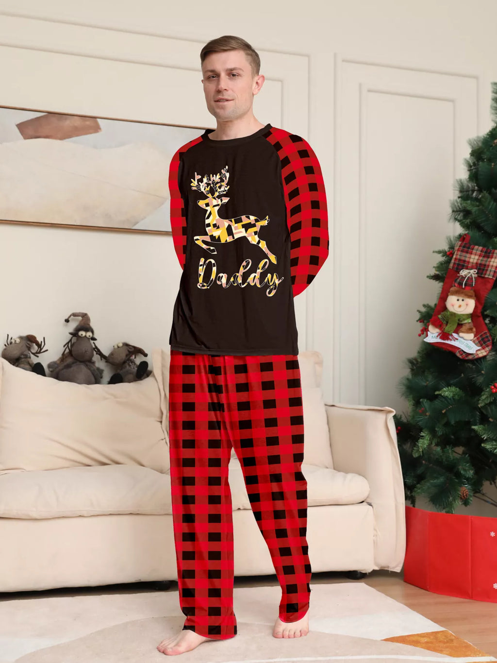 Man modeling a black gold-tone reindeer graphic pajama top with red plaid sleeves and matching pants.