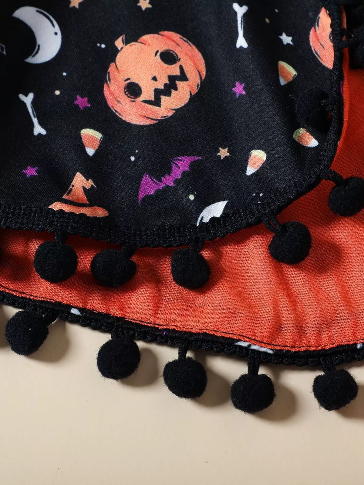 Ghost and pumpkin cape print with black pom-pom trim