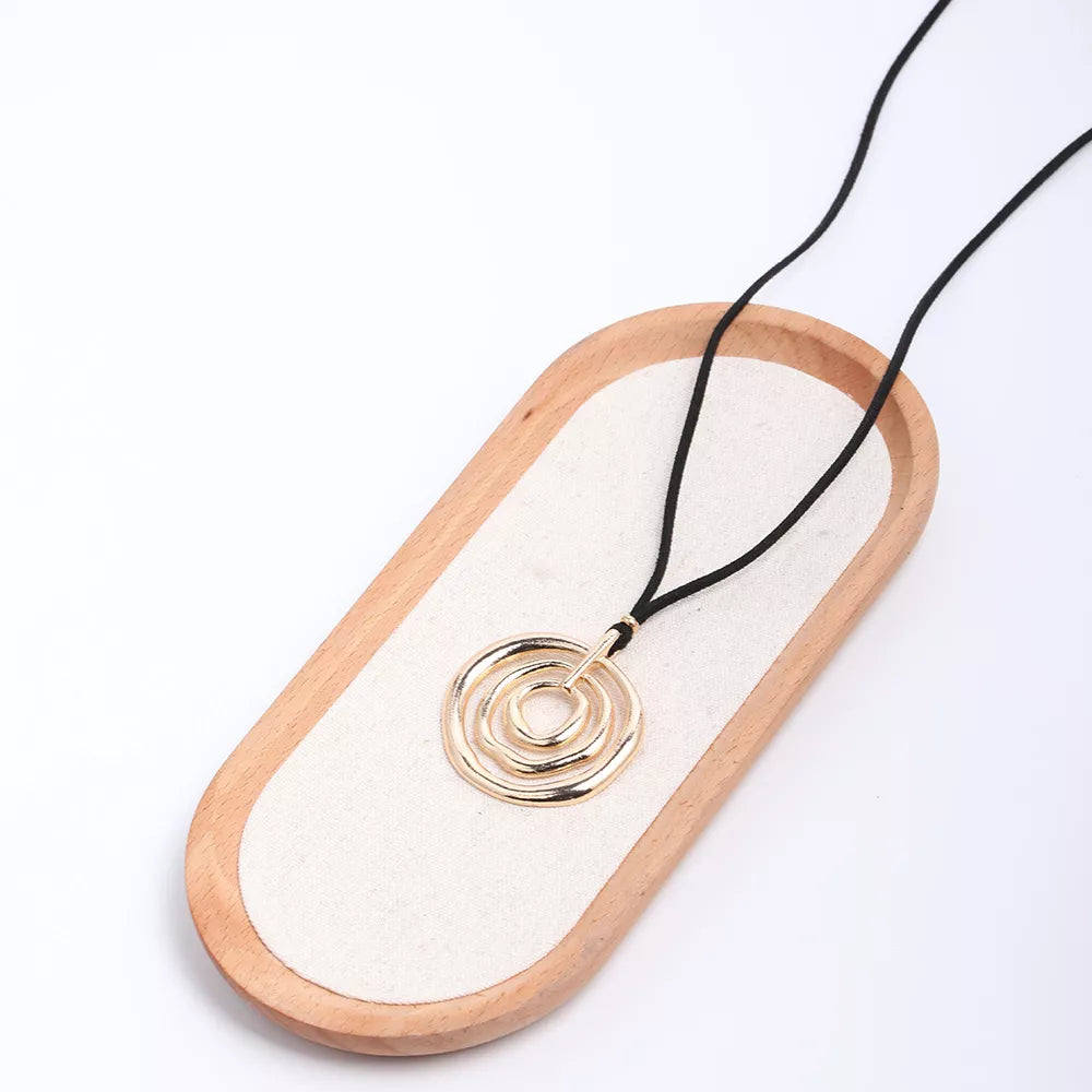 Long black cord necklace with a round gold-tone spiral pendant — detail view