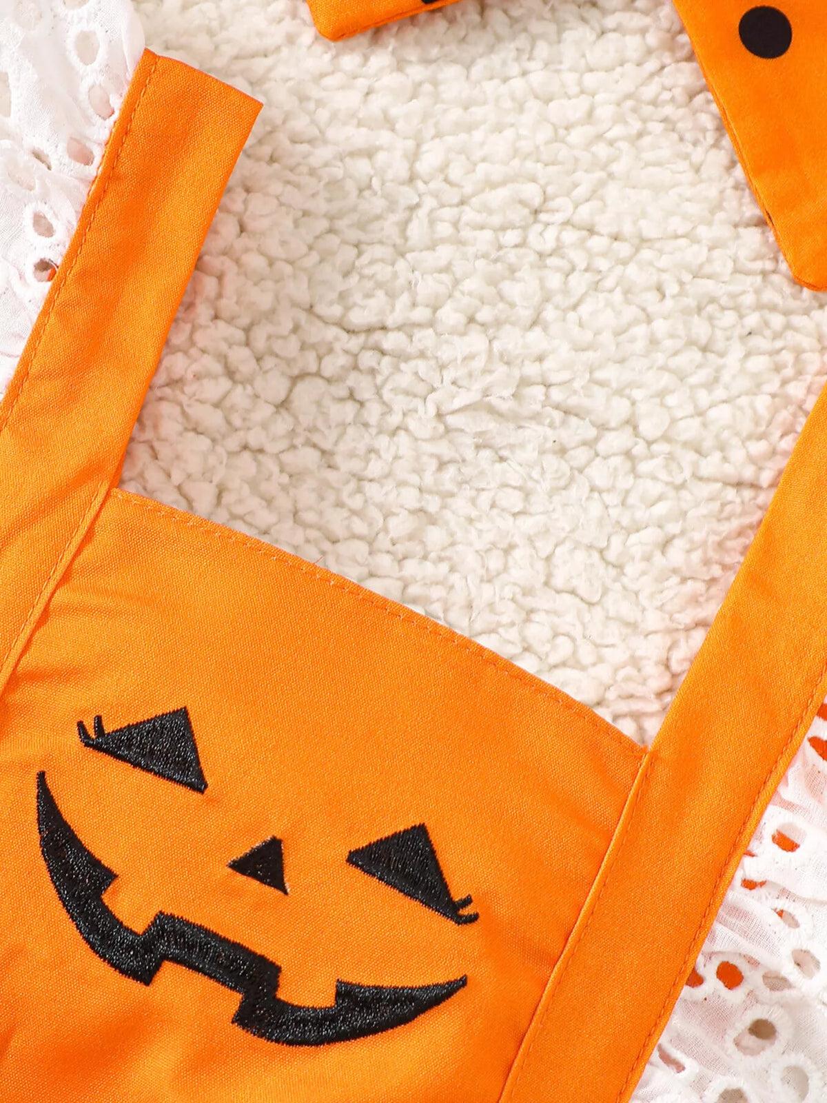 Close-up of the orange romper's black jack-o'-lantern face and white eyelet trim.