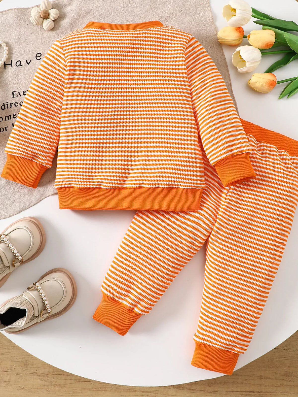 Orange striped ghost graphic pajama top and matching pants displayed flat