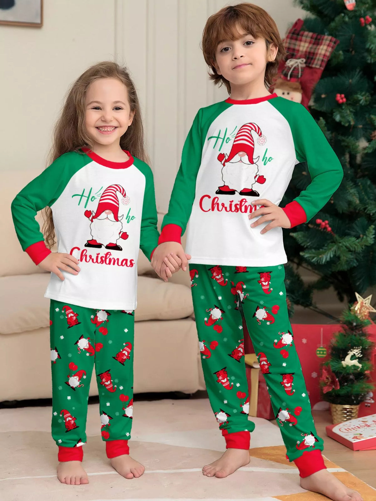 Two children wearing matching white Christmas tops with green sleeves and printed green pants.