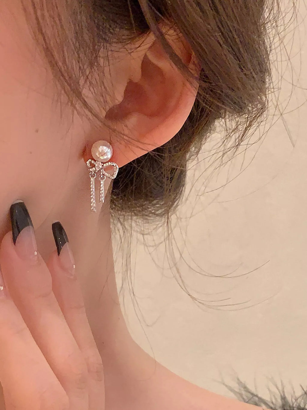 Bow-shaped drop earrings with pearl-like beads and chain tassels worn on a model