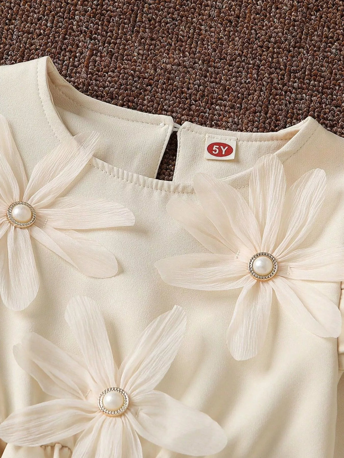 Close-up of the cream dress neckline, shoulder ruffles and pearl-look flower centers.