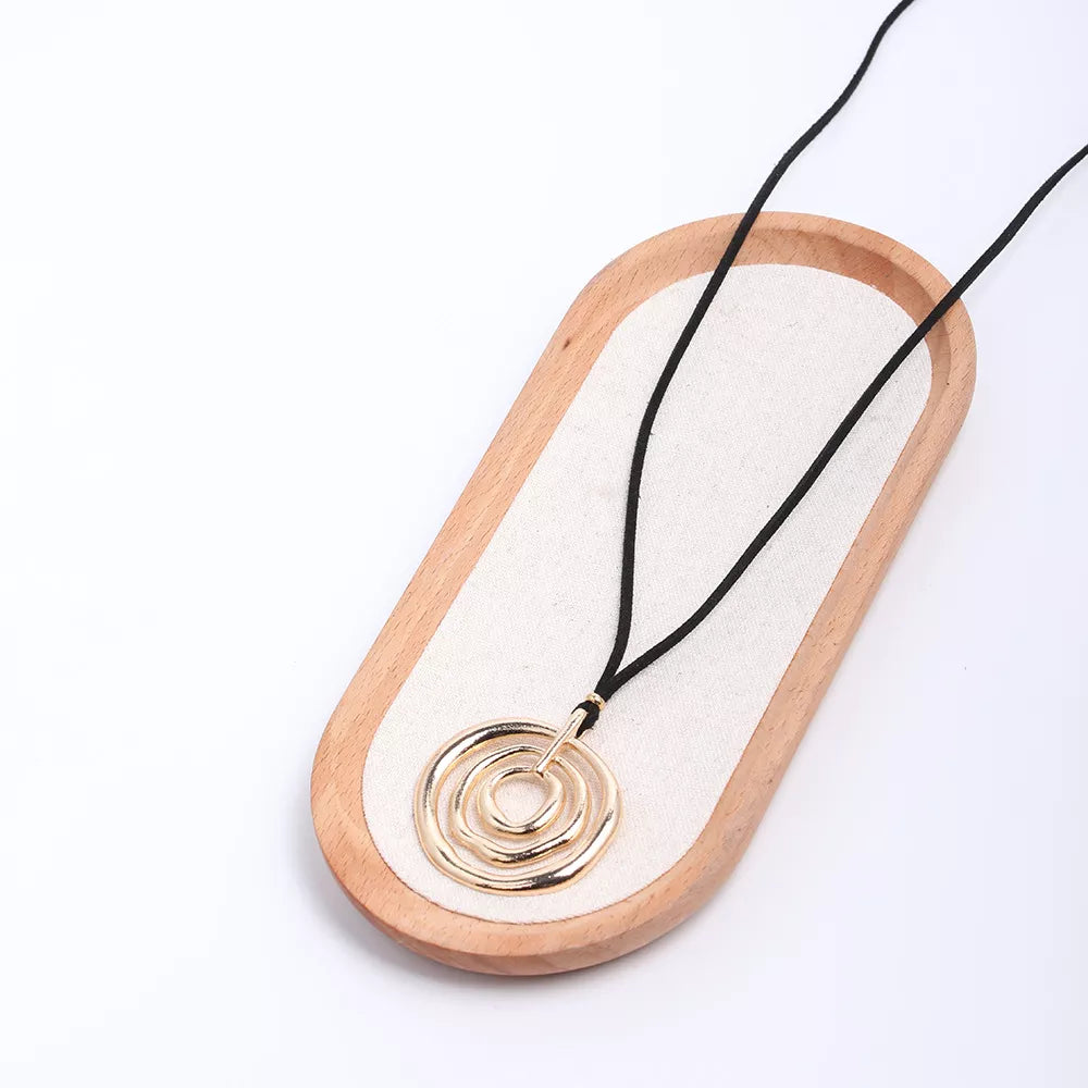 Long black cord necklace with a round gold-tone spiral pendant — detail view