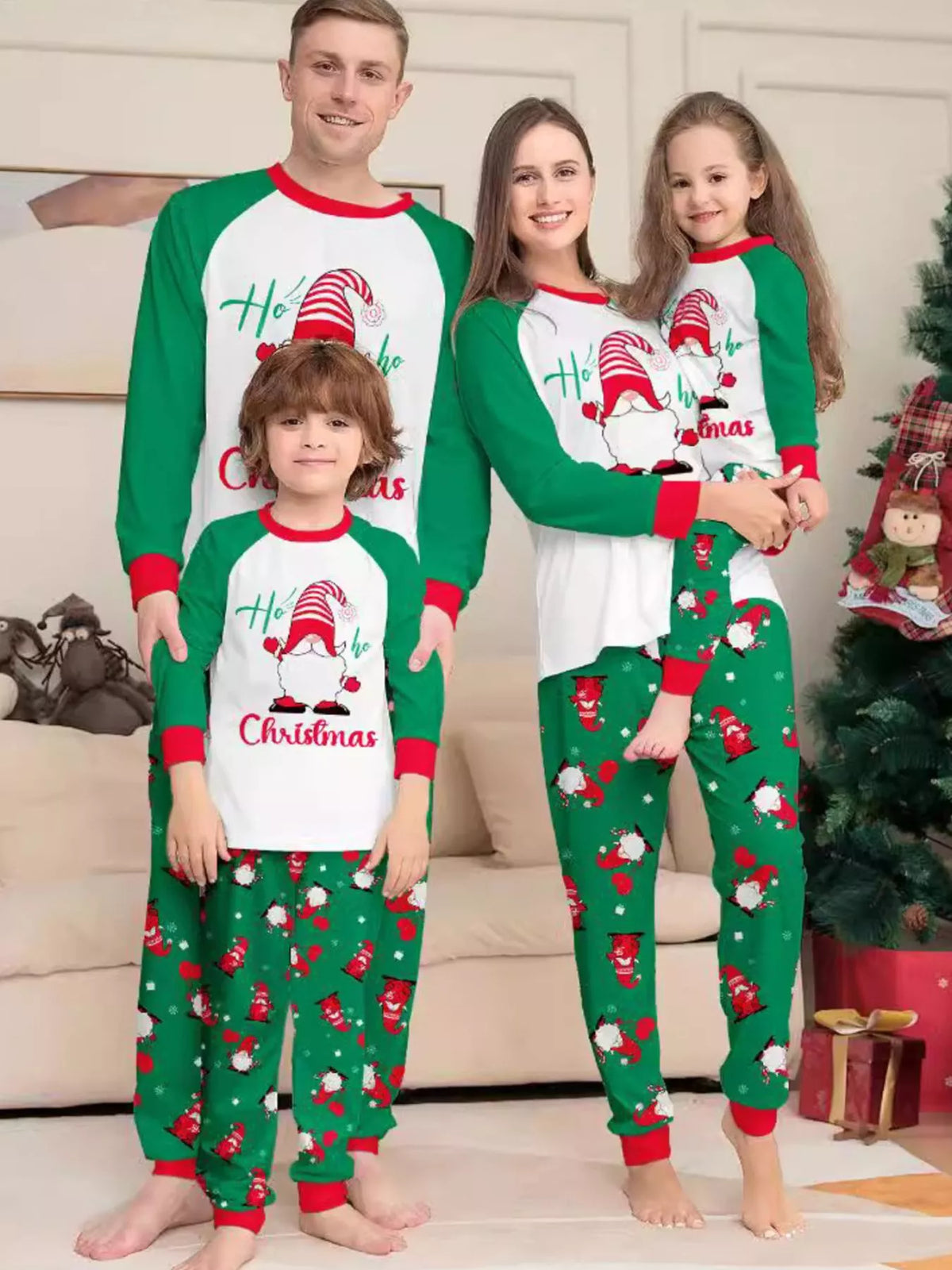 Family wearing white Christmas graphic tops with green sleeves and green printed pajama pants.